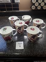 Top down and angle views of six Royal Kirkham floral mugs arranged on a dark kitchen countertop, showing the floral designs and mug shapes.