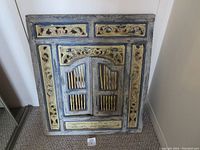 Front view of the wooden wall decor panel showing closed shutters and carved decorative elements.