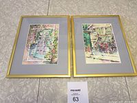 Two framed prints by artist Jill Louise Campbell, showing floral and architectural watercolor scenes in gold frames.