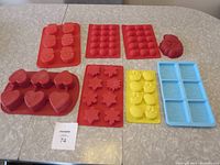 Photo showing eight colorful silicone molds with various shapes including hearts, flowers, stars, spheres, strawberries, and cartoon characters.