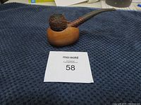 Vintage textured bowl tobacco pipe sitting atop wooden pipe holder on dark blue textured cloth with auction lot number.