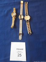 Three wristwatches on blue cloth background with a paper tagged 25