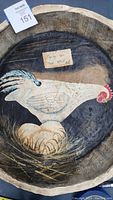 Photo of the hand painted hen artwork inside the wooden platter showing detail of the white hen, nest, and handwritten sign saying 'Laying Hen For Sale'.