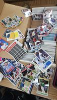 Wide view of baseball cards in a cardboard box, loose and in stacks showing a variety of players and card designs.