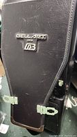 Close-up of Bell Art Japan brand logo on black hard travel golf bag case showing texture and wear.