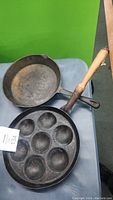 Overall view of both cast iron pans showing the skillet and ableskiver pan with wooden handle