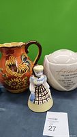 Front view of the ceramic rooster pitcher, the farmgirl-shaped porcelain shaker, and the white ceramic water fountain with the quote.
