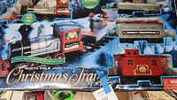 Photo showing full view of boxed North Pole Junction Christmas Train with detailed graphics, locomotive, coal car with Merry Christmas, animated elf car, and caboose in original packaging.