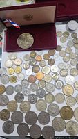 Collection of various international coins spread out with an Olympic medallion in a red velvet case.
