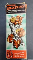 Front side of original Crackerjack box showing cartoon squirrels and tool cracking nut illustration