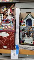 Photo showing Santa's Toy Factory music box and Christmas Streets lighted snow house displays side by side in their boxes.