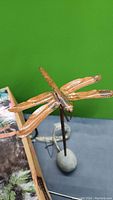 Copper dragonfly sculpture on tall post inserted into faux rock base, with original box and accessories visible in background
