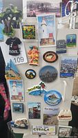 Photo showing 20 or more assorted 3D refrigerator magnets from various international locations including Antigua, Belize, Jamaica, Curacao, Amsterdam, and others attached to a metallic surface.