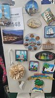 Photo showing sixteen assorted collectible souvenir magnets with various city and travel themes attached to a metal surface.