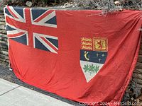 Full front view of flag laid flat showing Union Jack canton and coat of arms