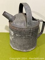 Full side view showing spout, handle, ribbed metal body with aged patina.