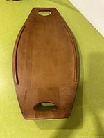 Top view of wooden surfboard-shaped tray on green surface, showing its full length, cutout handles, and groove details along sides.