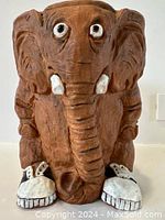 Front view of a brown ceramic elephant planter featuring large eyes, trunk, white tusks and white sneakers.