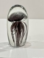 Glass paperweight showing jellyfish design in dark aubergine color with tiny bubbles on top inside the glass