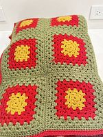 Folded hand crocheted blanket showing colorful granny square pattern in yellow, red, and olive-green.