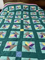 Full view of the hand made quilt showing floral blocks with graphic pattern on teal sashing.