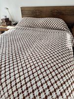 Bed cover displayed on a bed, showing brown and white repeating geometric pattern with texture.