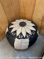 Front view of the round black and off-white leather ottoman with flower design on top.