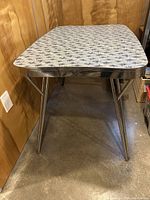 Rectangular mid-century modern laminate top table with chrome trim and angled legs shown from short end view.