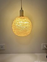 Yellow spherical pendant light hanging illuminated against a wall with visible power outlet below.