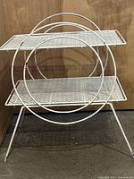 Full front view of the white 2-tier metal side table with circular handles and lattice shelves, showing overall form and design.