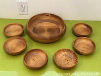 Front view of one large wooden bowl surrounded by six smaller wooden bowls, all with smooth finish and natural wood grain visible.