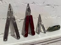 Five pocket tools displayed side by side, various sizes, some with pliers and plastic handles.