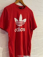 Front view of the red Adidas T-shirt featuring a large white trefoil logo and 'adidas' text on front.