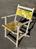 Side view of vintage folding lawn chair showing wood frame and floral fabric seat/backrest.