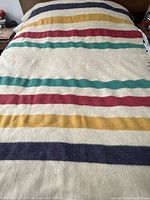 Full view of vintage Hudson Bay wool blanket with navy, yellow, red, and green stripes on cream background spread on a bed.