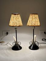Pair of vintage table lamps with black metal bases and mother of pearl shades illuminated, showing details of lamp bases and cords.