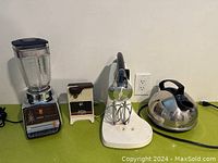 Vintage kitchen appliances including Sunbeam blender, electric can opener, electric kettle, and Sunbeam Mixmaster stand mixer on base with beaters