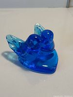 View of the blue glass figurine showing the two birds and the heart base, highlighting the glossy translucent blue glass.