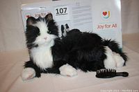 Photo of the cat with visible synthetic fur and comb included, lying beside its box.