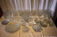 Full display of entire glassware set including goblets, plates, bowls, and lidded dishes sitting on table.
