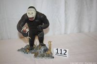 Full view of King Kong figure standing on a rocky base with a 'KING KONG' sign, holding a small bird. Background is a white cloth.