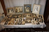 Wide view of the entire collection arranged on table, featuring a mix of framed, mounted, and loose vintage black and white photographs including wedding scenes and family portraits.