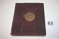 Front cover of the book showing burgundy cloth hardback with gilt-stamped city emblem and blind-stamped illustration, edges worn.