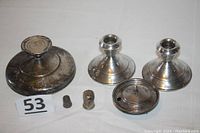 Photo showing all six sterling silver items arranged on white fabric including the pair of candlestick holders, weighted compote base, small base with lid, thimble, and pepper shaker with lot number card.