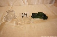 Three vintage glass automobile-shaped candy containers displayed on fabric surface with number 19.