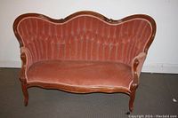 Front view of the antique wing back Victorian sofa in reddish-pink velvet upholstery with wooden frame.