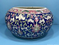 Front and side view of round vintage Chinese porcelain planter with detailed floral patterns on blue background.