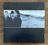 Front cover of The Joshua Tree album by U2 showing band members against a desert background.