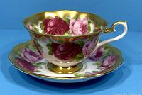 Tea cup and saucer set with floral rose design and gold accents on a blue background.
