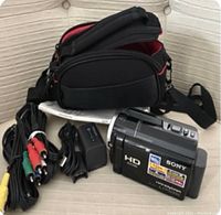 Sony HDR-XR160 camcorder with accessories including two batteries, RCA cables, computer cable, manual and carrying bag displayed on couch.